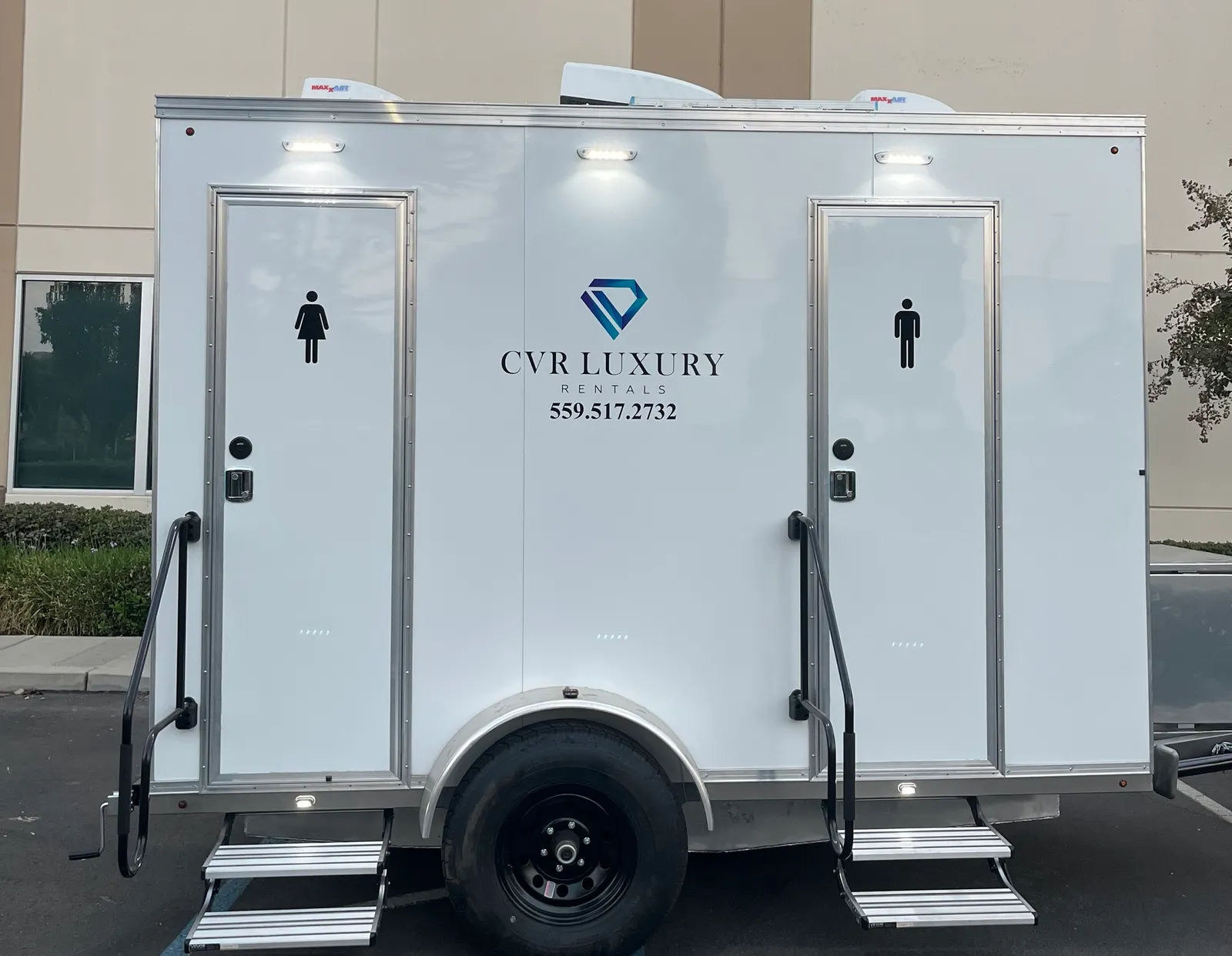 The CVR Luxury Rentals restroom trailer at dusk with its lights on, showing separate women's and men's entries with steps and handrails