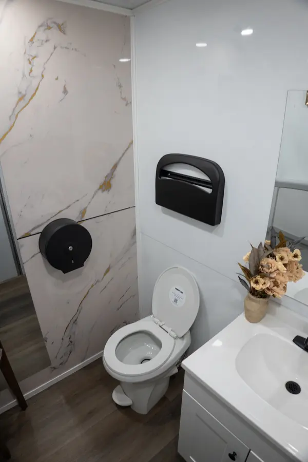 Flushing toilet in front of a white marble wall with gold veining, with a seat cover dispenser and flowers