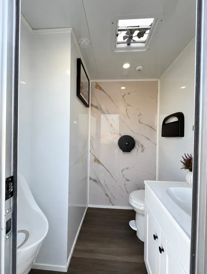 Men's suite inside the CVR trailer: urinal, flushing toilet against a marble and gold accent wall, and a white vanity