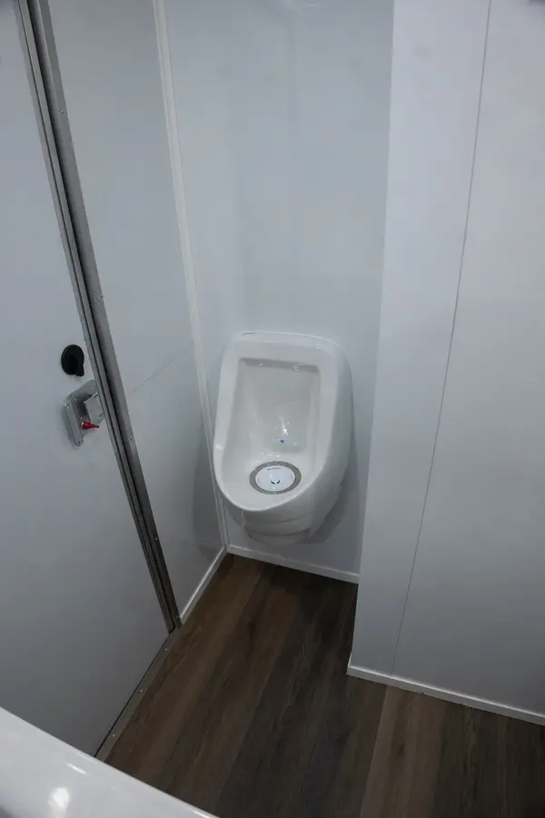 Wall-mounted urinal in the men's suite with wood-look flooring