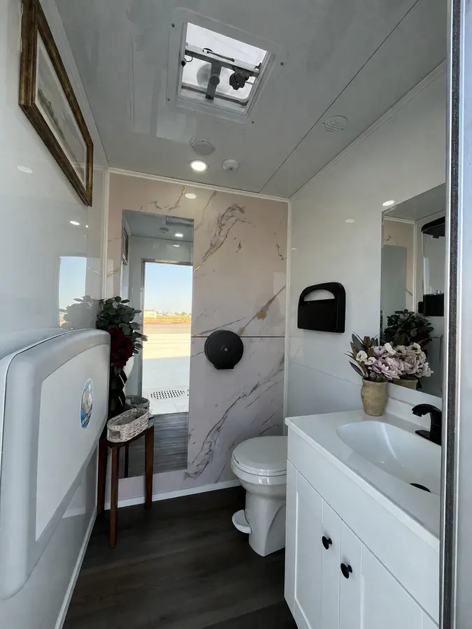 Women's suite inside the CVR trailer: white vanity, marble and gold accent wall, full-length mirror, framed art, and a fold-down baby changing station
